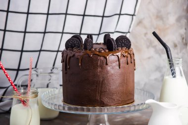 Vintage gri bir arka plan üzerinde parlak tübüllerin ile süt ile gemi arasında bir cam stand bisküvi ile çikolatalı kek. Gurme pasta kavramı