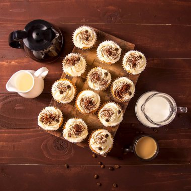 Tiramisu kek kakao tozu ve süt, krema ve bir fincan kahve sürahi yanında ahşap bir gemide kahve taneleri ile dekore edilmiştir. Üstten görünüm, düz yatıyordu