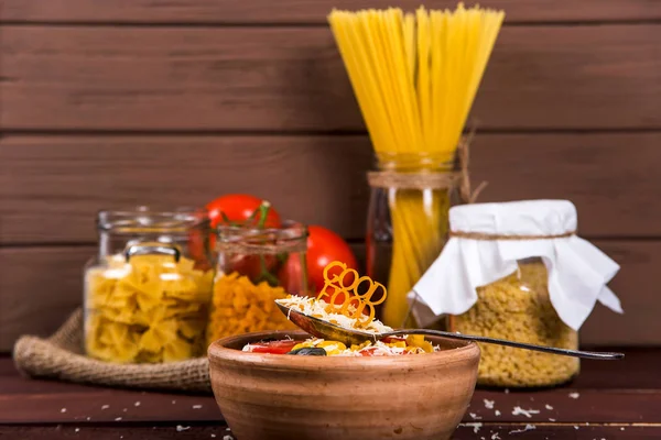 Good food is lined with pasta on a spoon near a plate with ready-made pasta with tomato, basil and parmesan on a wooden rural table. Healthy Vegan Nutrition Concept