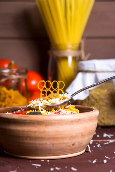 Good food is lined with pasta on a spoon near a plate with ready-made pasta with tomato, basil and parmesan on a wooden rural table. Healthy Vegan Nutrition Concept