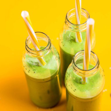 Yeşil smoothies parlak sarı bir arka plan üzerine boruları ile üç cam şişelerde. Sağlıklı gıda detoks kavramı. Kopya alanı