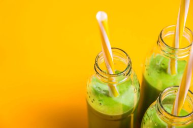 Yeşil smoothies parlak sarı bir arka plan üzerine boruları ile üç cam şişelerde. Sağlıklı gıda detoks kavramı. Kopya alanı