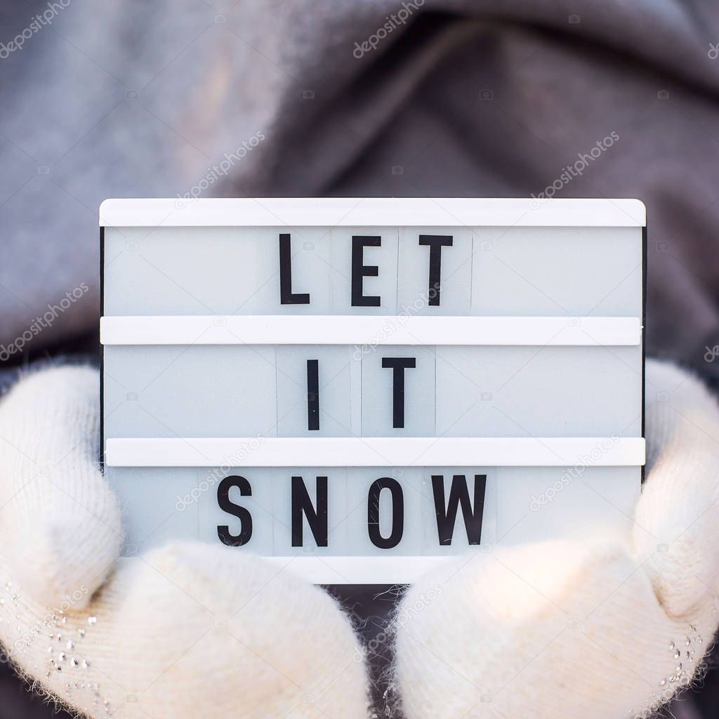 Let it snow it is written on a decorative lamp held by a woman in a gray scarf and white mittens