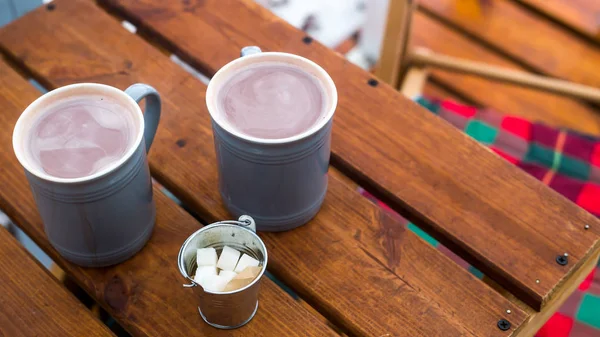 Two cups of cocoa and sugar bucket on a wooden table on the outdoor winter terrace. Hot sweet drink