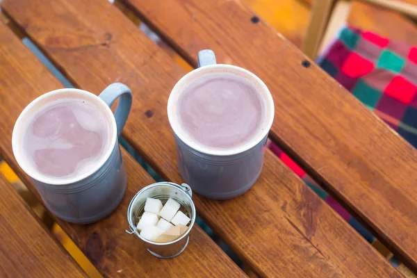 Two cups of cocoa and sugar bucket on a wooden table on the outdoor winter terrace. Hot sweet drink
