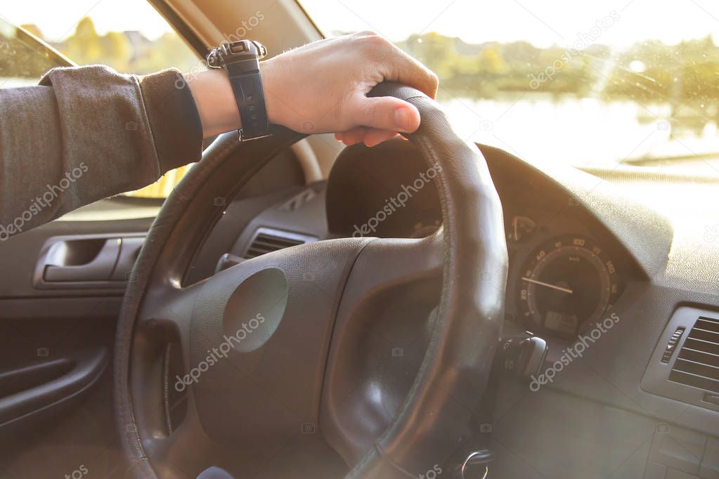 The hand of a Caucasian man on the steering wheel of a car. Traveling by car on a bright sunny day, learning to drive a car concept