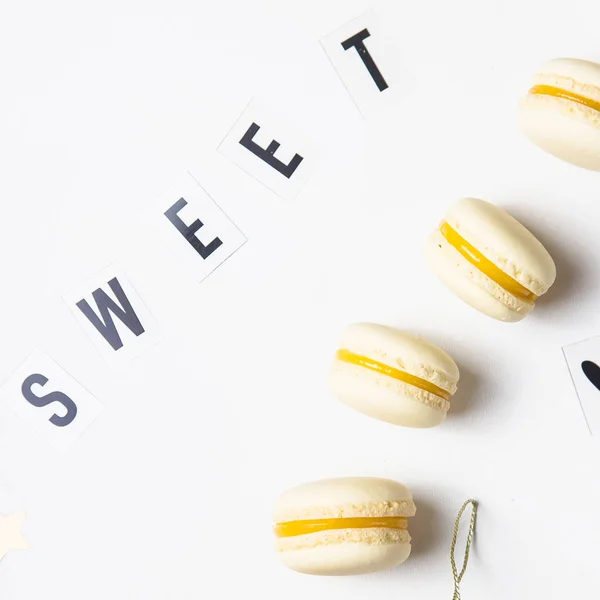 The word sweet is laid out in black letters on a white background next to yellow lemon macaroons. Festive dessert. Top view, flat lay