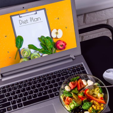 Dizüstü bilgisayar masaüstü yakınındaki sebze salatası kase. Üstünde belgili tanımlık perde - bir diyet kilo kaybı Pazartesi için planlama