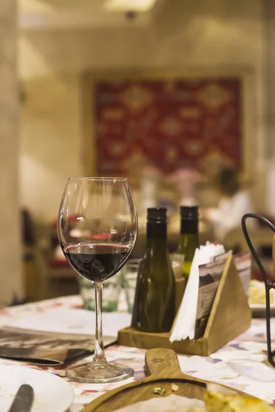 A glass of red wine on a table in a restaurant where a group of friends or family dine