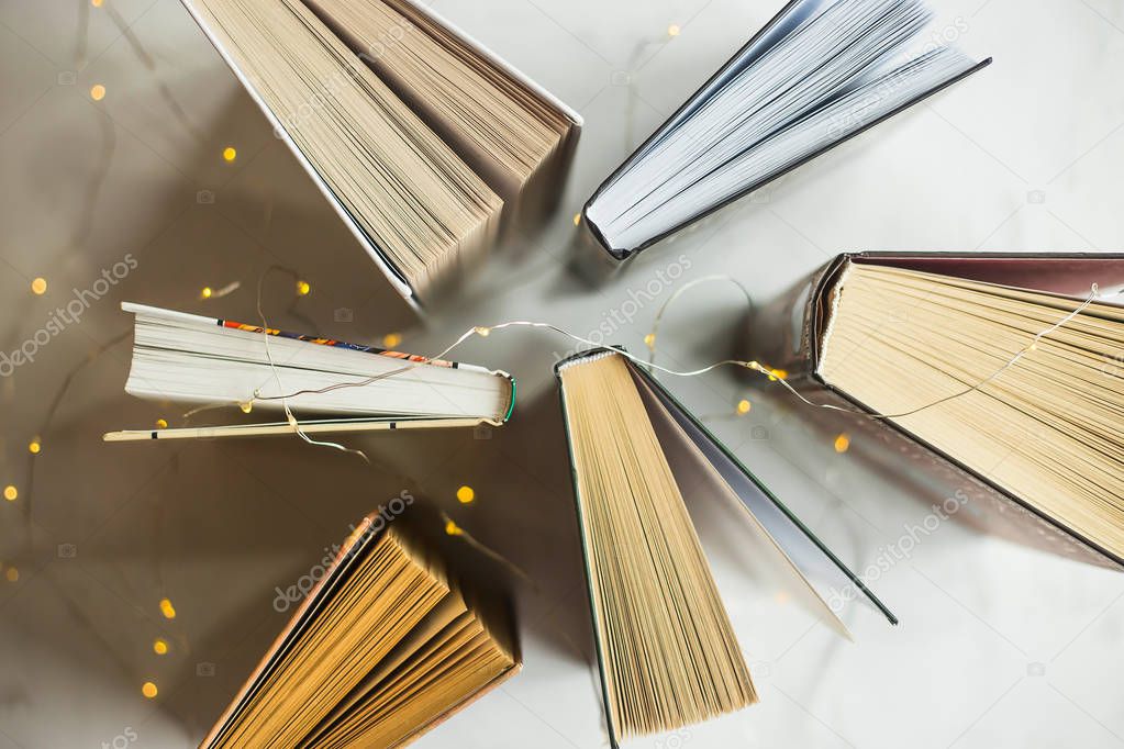 Books stand on a table with yellow lights of a garland. Reading concept. Top view, flat lay