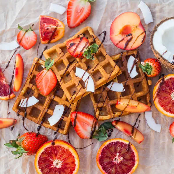 Wafels met aardbeien, kokos, pruim en oranje met chocolade — Stockfoto