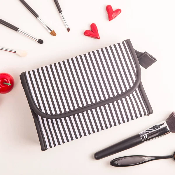 Black and white cosmetic bag among makeup brushes and bright red things on a white background. Minimalistic and stylish cosmetics. Top view, flat lay