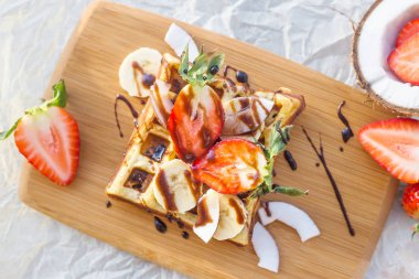 Belçika waffle meyve ve çikolata sosu ile güzel bir ahşap tahta üzerinde servis edilir. Üstten Görünüm, düz yatıyordu