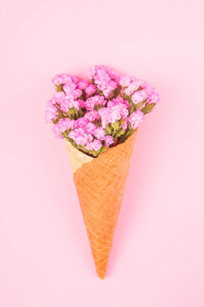 Beautiful pink flowers in a waffle cone for ice cream on a bright pink background. Top view, flat lay