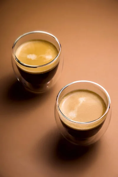 Café preto com espuma em copos modernos em um fundo liso — Fotografia de Stock