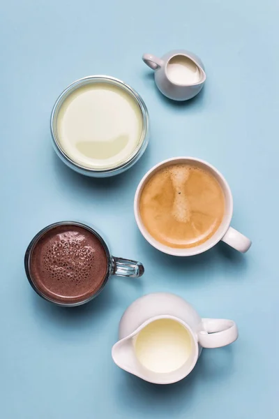 Coffee, cocoa and matcha with white creamers of milk on blue