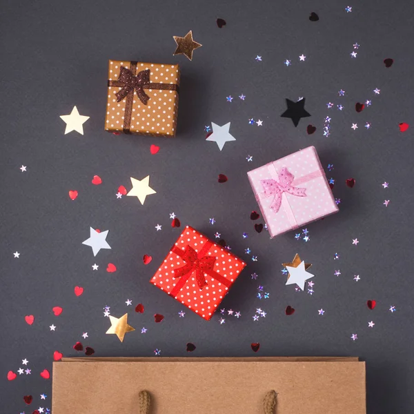 Kraft paper bag on bright dark background. With gift boxes and confetti. Black friday christmas gift preparation concept.