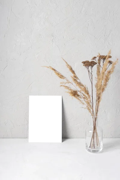 Mock up postcard which stands on a gray background next to a vase with dried flowers in the style of eco minimalism.