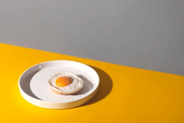 Œuf frit sur une assiette blanche sur fond jaune avec ombres . — Photo