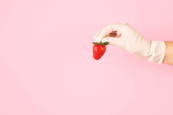 Hand i handske håller jordgubbar på en rosa bakgrund. — Stockfoto