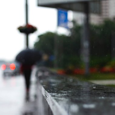 Şehir kaldırımındaki korkuluklara yağmur damlaları düşer. Bulanık şemsiyeli bir adam. Sonbahar havası