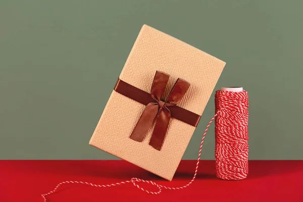 A balancing Christmas present next to a skein of red and white rope. — Stock Photo, Image