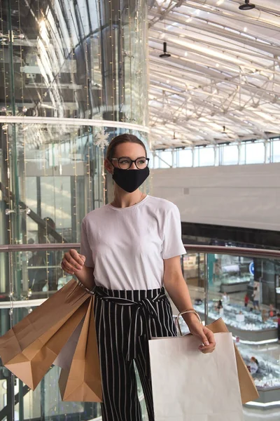 Дівчина в окулярах і захисна маска в торговому центрі з покупками — стокове фото