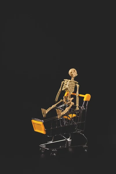 Esqueleto de Halloween en un carro de supermercado sobre fondo negro —  Fotos de Stock
