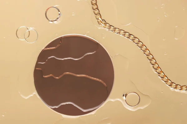 水滴の間にベージュの背景にラウンドミラーと女性の金のアクセサリー トップ表示流行のレイアウト — ストック写真
