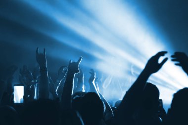 İnsan aydınlık pop-rock konserinde sahne önünde siluetleri. El jest boynuzları. Şok edici. Bir kulüpte parti