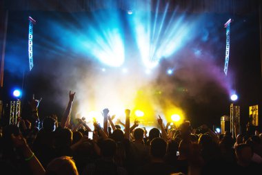 İnsan aydınlık pop-rock konserinde sahne önünde siluetleri. El jest boynuzları. Şok edici. Bir kulüpte parti