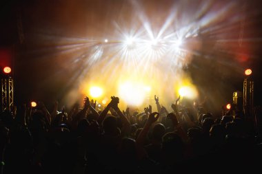 İnsan aydınlık pop-rock konserinde sahne önünde siluetleri. El jest boynuzları. Şok edici. Bir kulüpte parti