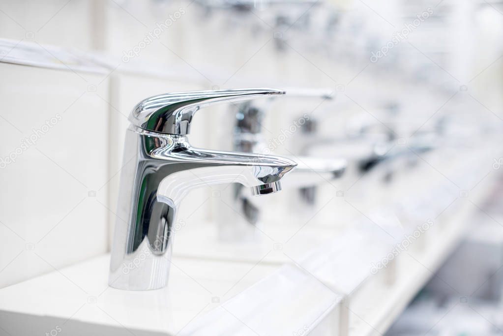 Bathroom faucet in the store. Showcase in white with chrome taps in a building supermarket. Soft focus