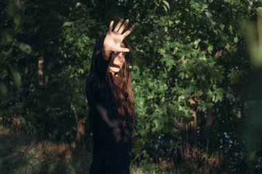 dreadlocks yeşil çalılar bir arka plan üzerinde siyah giysili genç kızla. güneş ışığı parmaklarının arasından geçer. hippiler doğada
