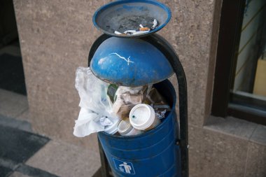 mavi metal çöp kovası kaldırımda şehirde bir kül tablası ile taşan