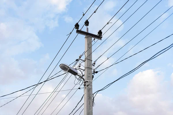 Lots of wires and cables and a street lamp with a blue sky background