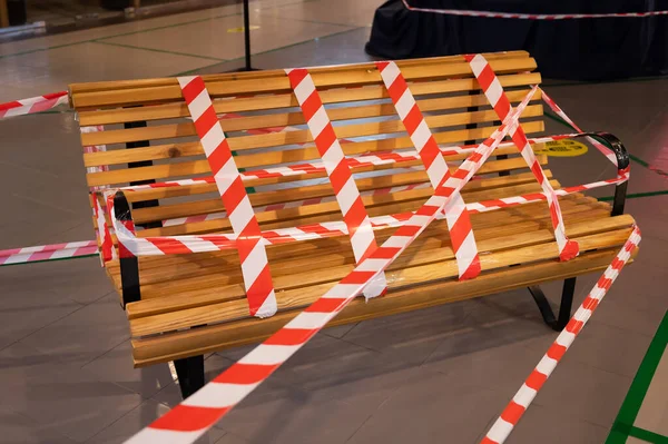 Wooden bench in the mall is surrounded by a warning tape. ban on staying in a public place. Social distance during coronavirus with a public bench covered with barrier