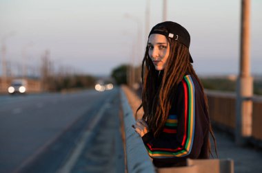 Şapkalı yaramaz kız yolda otostop çekerken bir araba yakalıyor. Hippi bütçesi gezisi