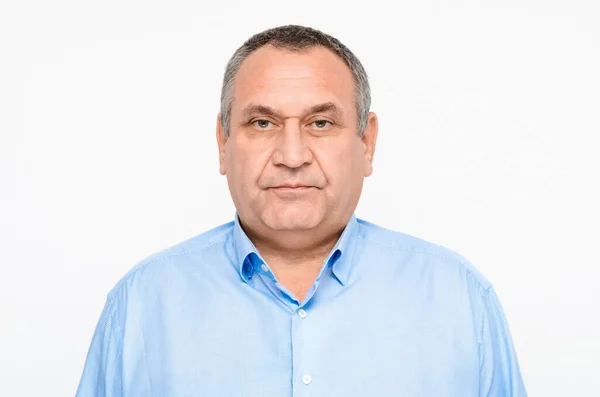 Beyaz arka planda mavi gömlekli, gri saçlı ve kaşlı yetişkin bir adamın portresi. Çift çene. Şişko adam. İş adamı