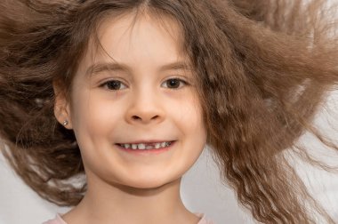 Ön dişi olmayan, dalgalı saçlı tatlı bir kız gülümsüyor. Yumuşak saçlı güzel bir kızın portresi.