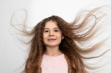 Kahverengi gözlü, dalgalı saçlı güzel bir kız süt dişini kaybetti. Rüzgarda mutlu bir anaokulu öğrencisi