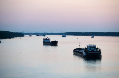 Mavnalar, balıkçılık ve ticari gemiler gün batımında nehrin arka planında tellerin ve direklerin karşısında. Şehrin sanayi bölgesi. port