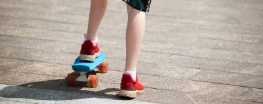 Plastik bir kaykayın üzerinde kırmızı spor ayakkabılı genç bir kaykaycının bacakları. Adam sörf tahtasında ata binmeyi ve dengeyi öğreniyor.