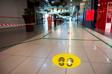 Alışveriş merkezinde ayak izi olan sarı etiket salgın sırasında sosyal mesafeyi anımsatıyor. Çalıntı kırmızı-beyaz bantlar kapalı dükkanlar