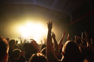 Güzel bir grubun rock konserinde dans eden kalabalığın elleri. Sahnede sisli bir müzisyenin silueti. müzik festivali afişi