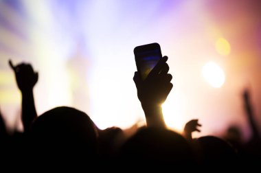 En sevdiği grubun konserinde video ve hafıza fotoğrafı çeken bir hayranın elindeki akıllı telefon ekranı. Sahne ışıklandırmalı bir müzik festivalinin atmosferi