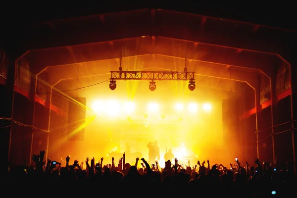 Sahnede parlak spot ışıkları ve dans eden kalabalıkla dolu bir müzik grubunun siluetleri. Bir müzik festivalinin atmosferi. konser posteri
