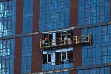 İnşaat asansöründeki üniformalı işçi gökdelene yeni pencereler takıyor. Ofisleri olan iş merkezlerinin onarımı ve bakımı.
