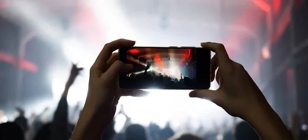 girl hands at a concert shoots videos and photos of the crowd and the stage with a group on a smartphone. music festival in the club. joyful moments