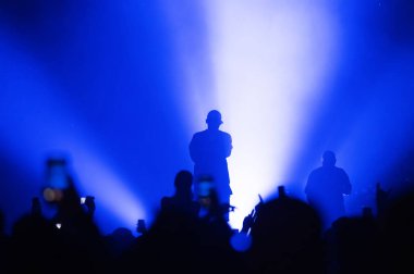 Müzisyenlerin silueti mavi bir spot ışığı altında sahnede. Dans eden bir kalabalığın olduğu bir müzik festivalinin atmosferi. Görüntü. Seçici odak